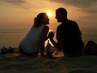 Konturer av par som sitter och tittar på varandra och håller hand på en sandstrand i solnedgången